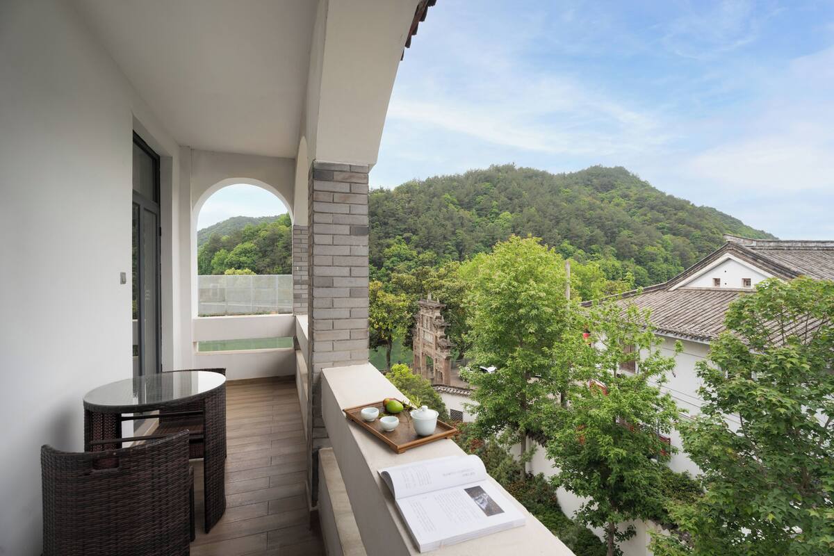 Un balcon avec une table en verre, des chaises en osier et un plateau sur lequel se trouvent un bol, une tasse et un fruit.