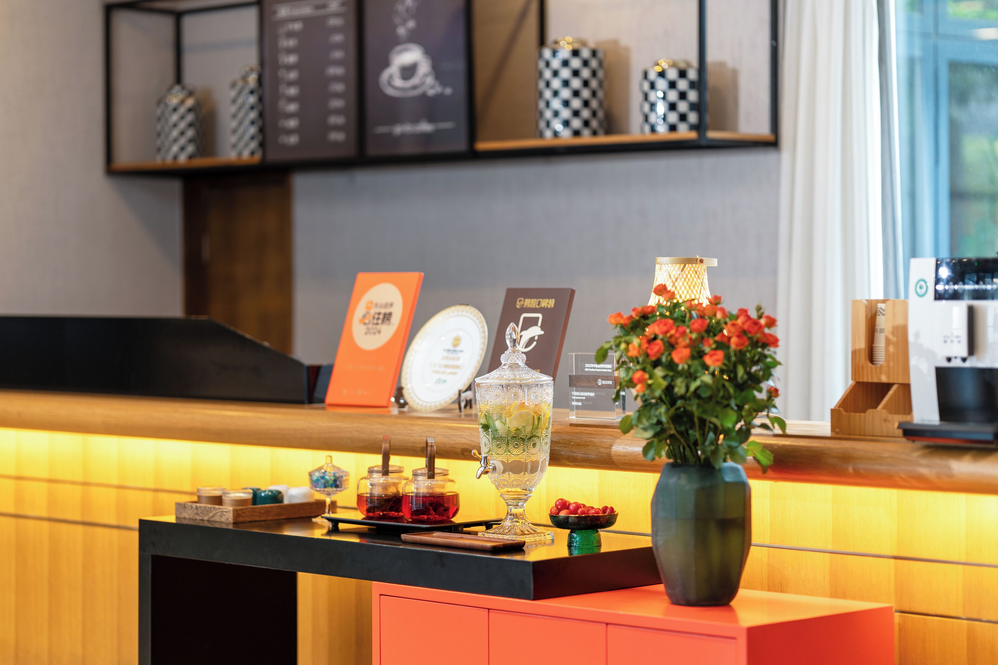 Una mesa de recepción con un florero, una cafetera y un panel de menú.
