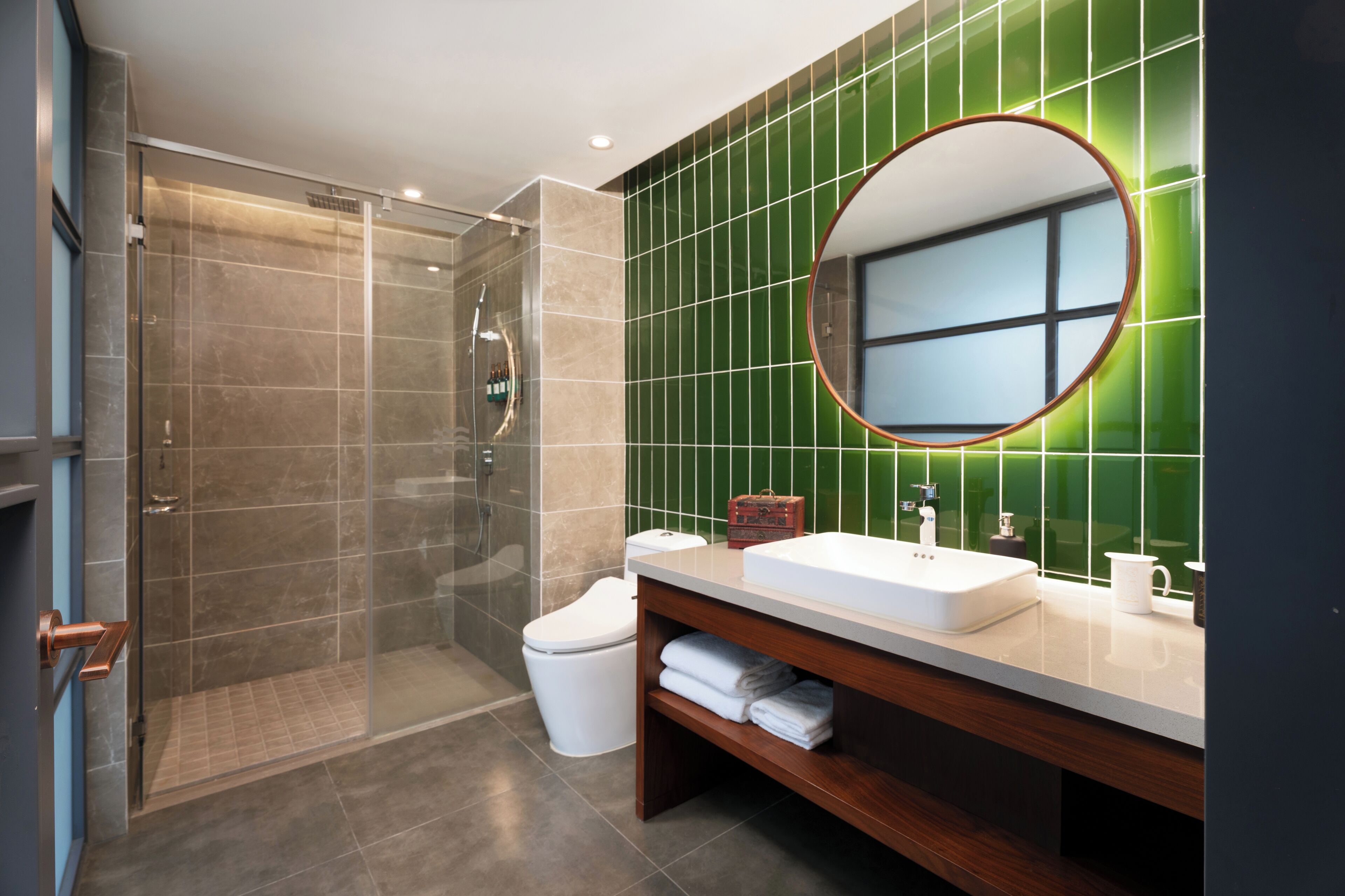 A modern bathroom with a glass-enclosed shower, a white sink, and a green-tiled wall.