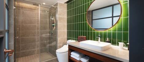 A modern bathroom with a glass-enclosed shower, a white sink, and a green-tiled wall.