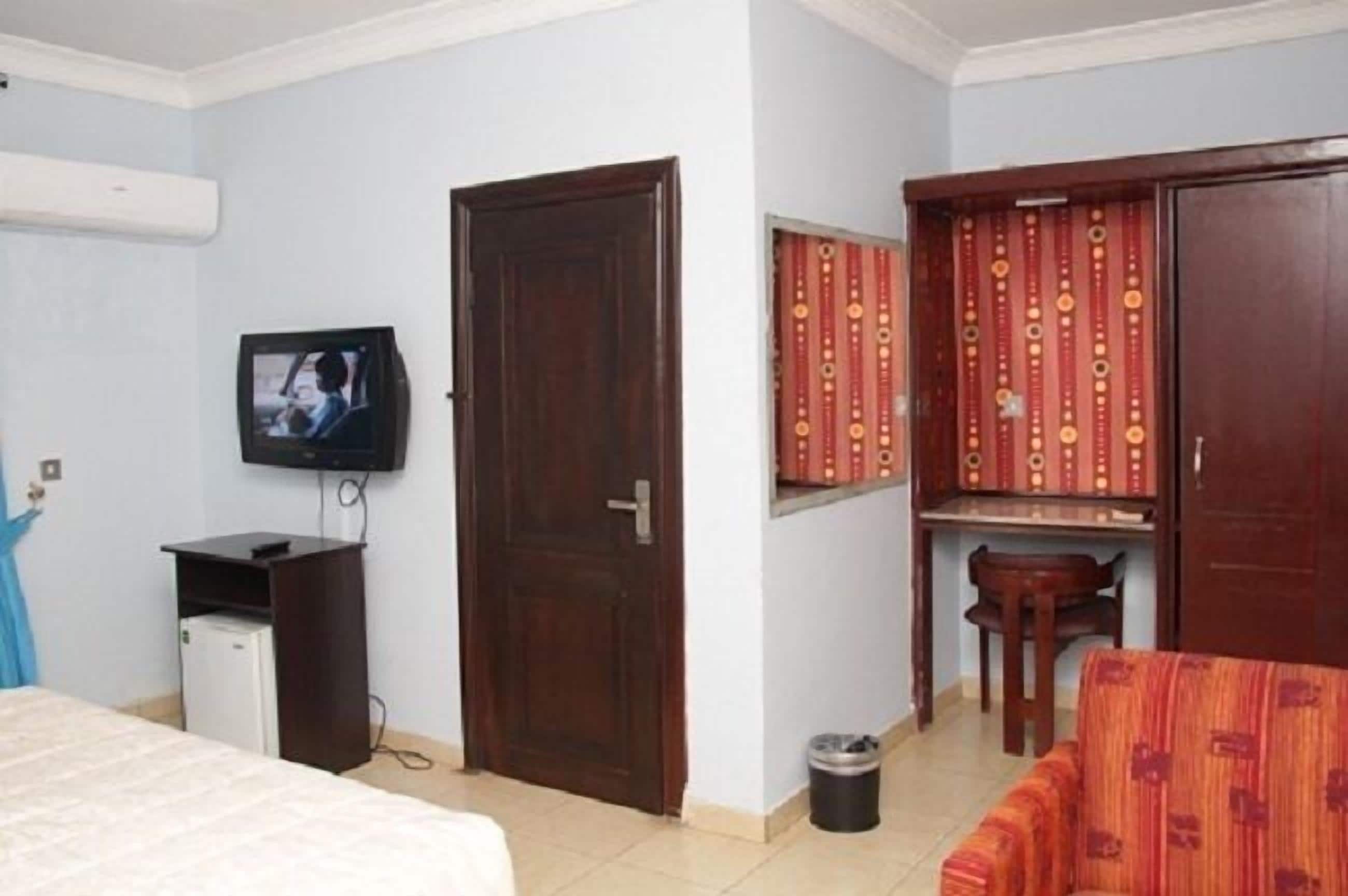 A hotel room with a bed, a desk with a chair, a television, and a wardrobe.