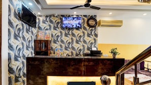 Una zona de recepción con pared con diseño de mármol, un televisor de pantalla plana, un reloj y un equipo de aire acondicionado.