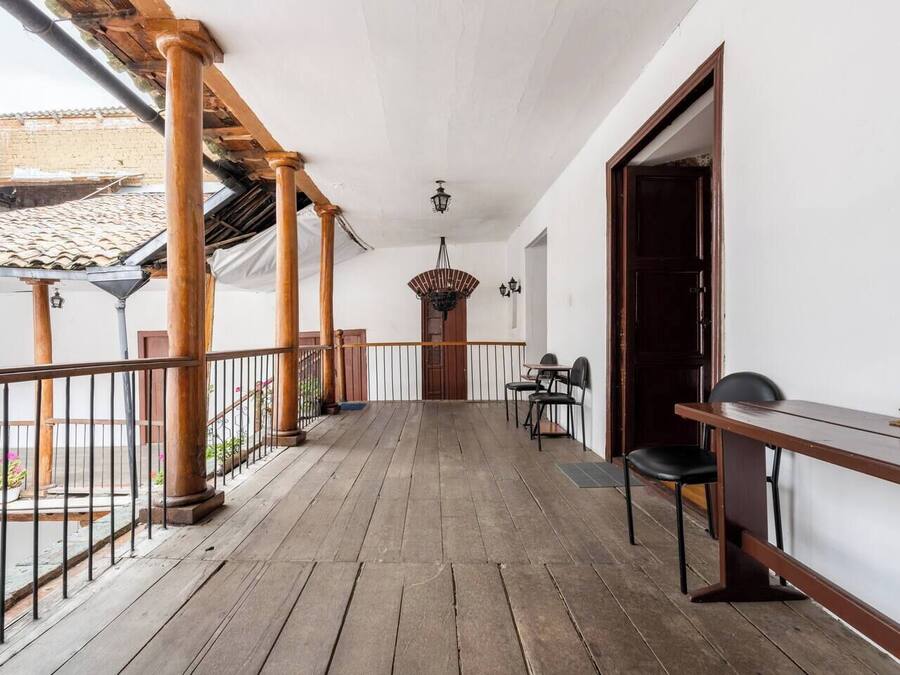 Un balcón de madera con barandilla, una mesa y sillas.