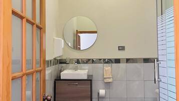A compact bathroom with a wooden door, a round mirror, a sink, a toilet, and a shower area.
