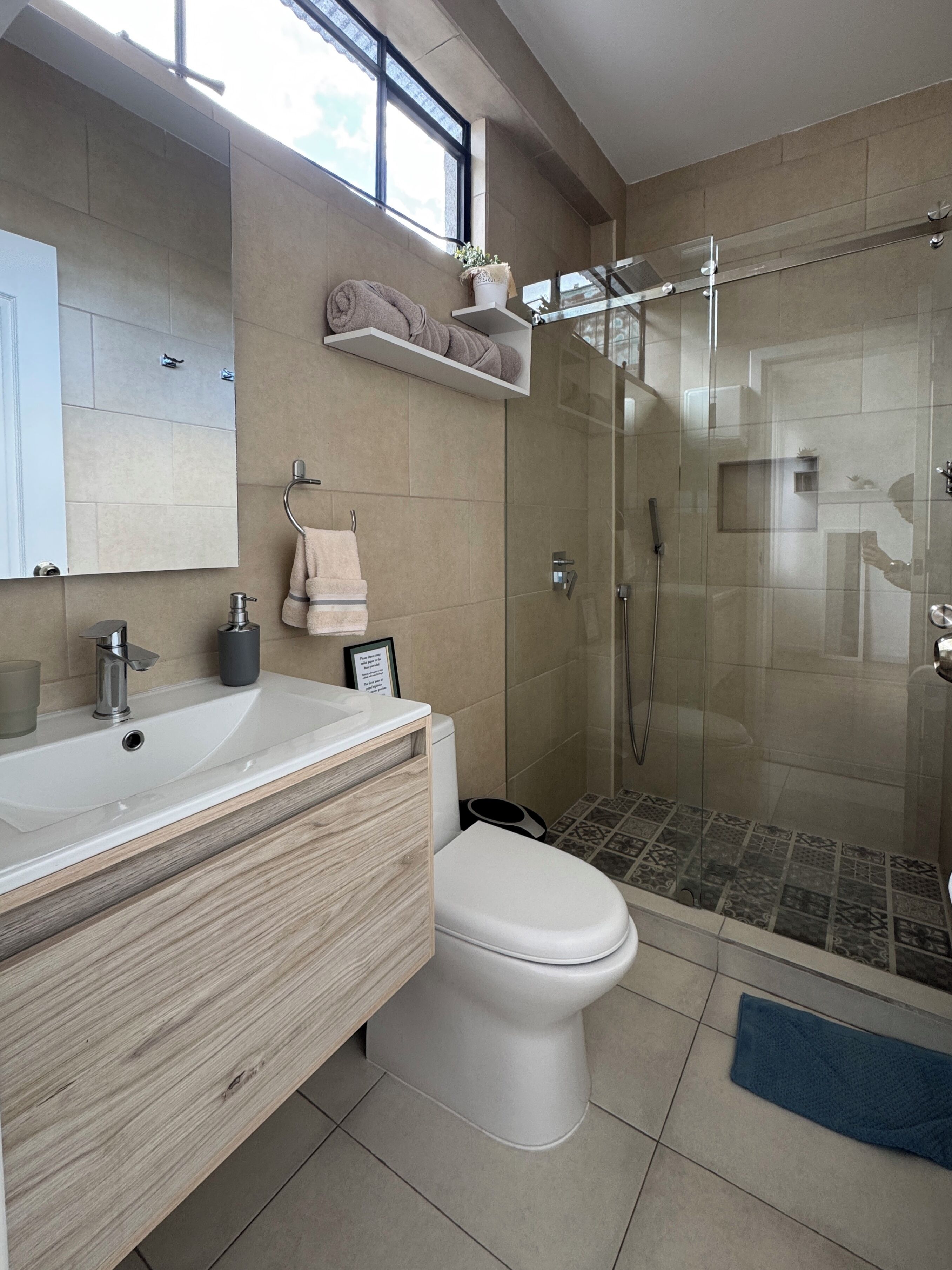 A modern bathroom with a glass-enclosed shower, a wooden vanity, and a toilet.