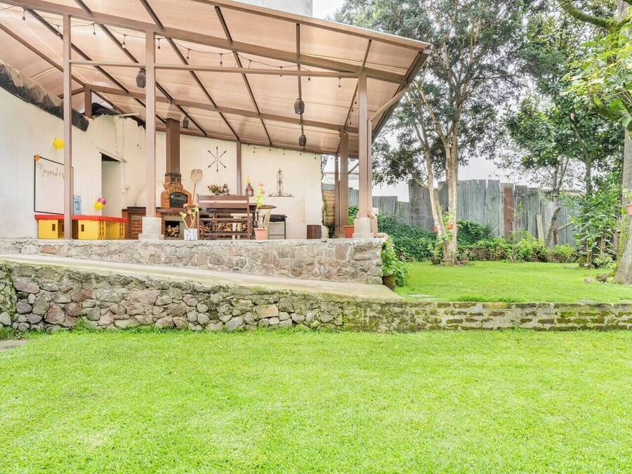 A covered outdoor area with a stone wall, a brick fireplace, and a wooden table.