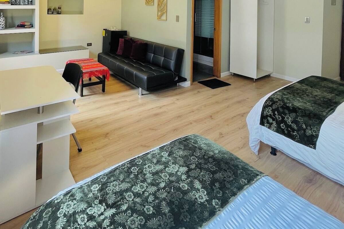 A modern, well-lit room with a sofa, two beds, a desk, and a wardrobe.