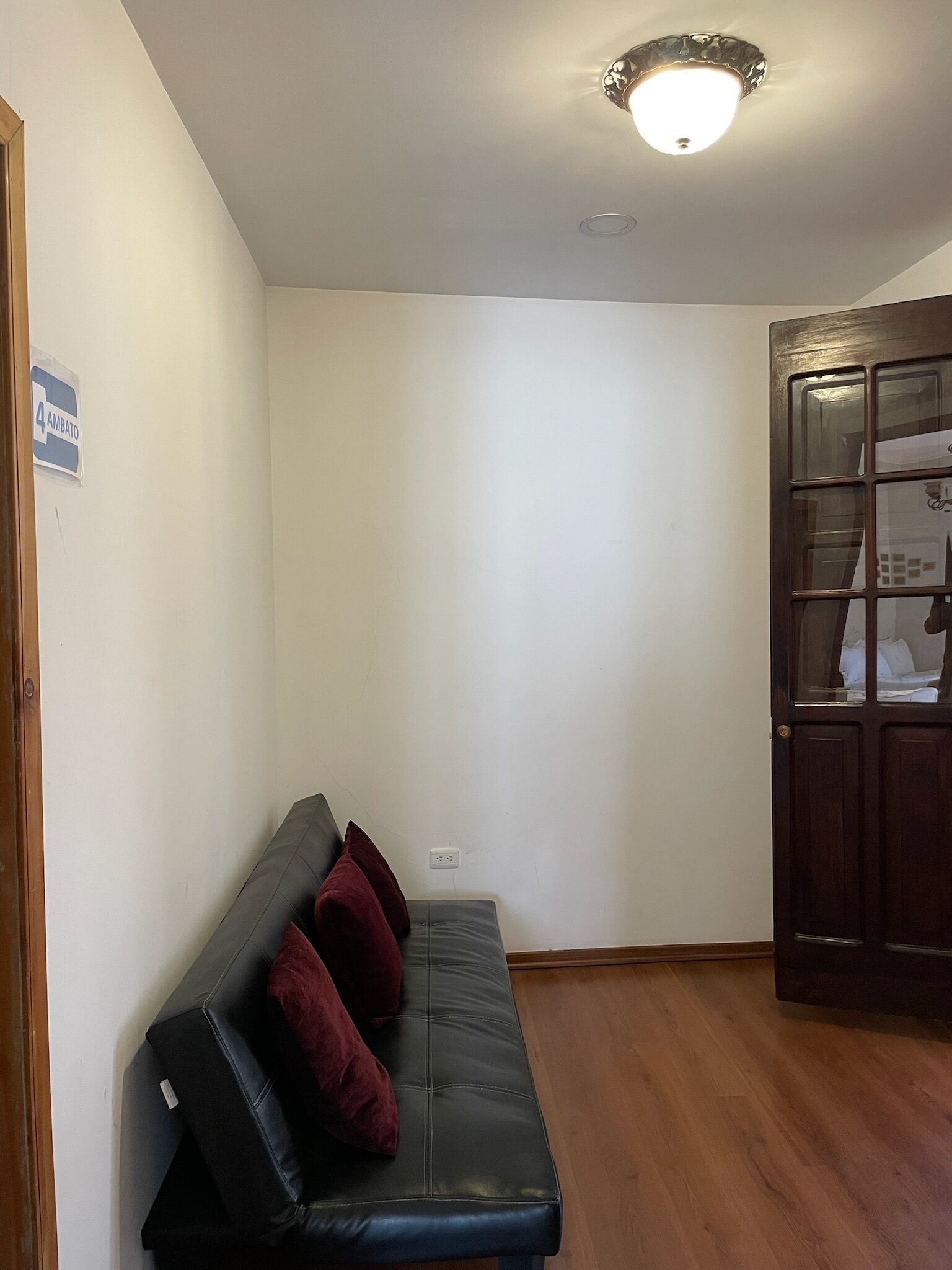 Una habitación con un sofá de cuero oscuro, una puerta de madera y una pared blanca con un letrero que dice "4 AMBATO".