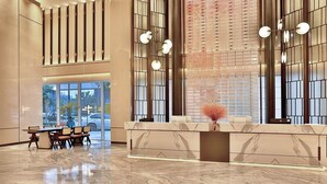 Una hall moderna con una reception in marmo, area salotto e ampie finestre.