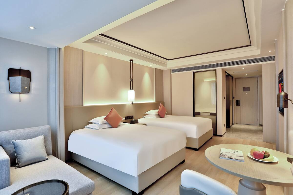 Een moderne hotelkamer met een bank, twee bedden, een glazen tafel en een eethoek.