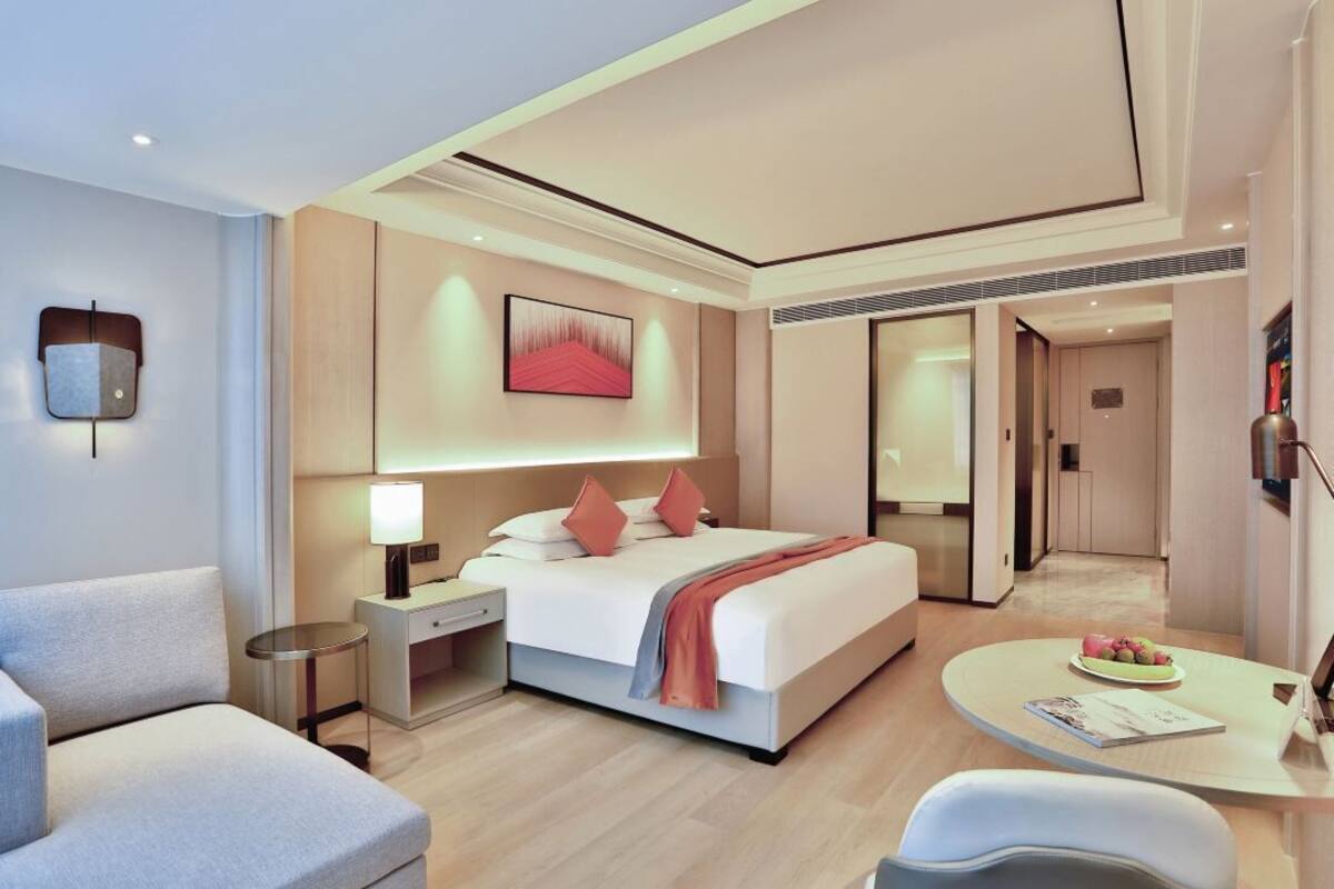 Een moderne hotelkamer met een bed, nachtkastje, lamp en een klein zithoekje met een tafeltje.