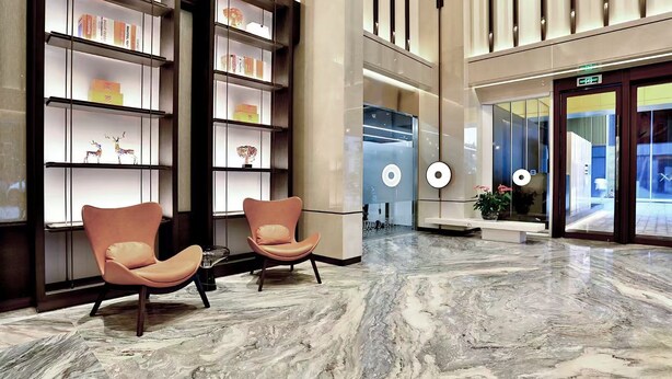 Una hall moderna con pavimento in marmo, due poltrone confortevoli e un ascensore in vetro.