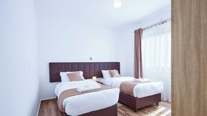Habitación de hotel con dos camas, piso de madera y un ventanal grande con cortinas.