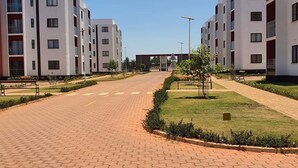 Un moderno complejo de apartamentos con un camino peatonal central, rodeado de céspedes cuidados y pequeños árboles.