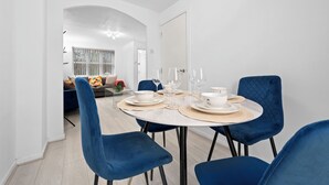 A dining area with a round table set for four, blue velvet chairs, and a view into a living room with a sofa and a dining table.