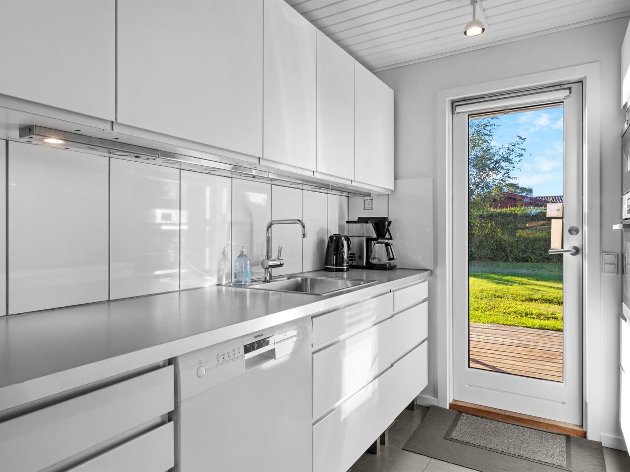 A modern kitchen with white cabinetry, a stainless steel sink, and a coffee maker.