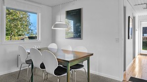 Een moderne eetruimte met een houten tafel en witte stoelen, een hanglamp en een poster aan de muur.