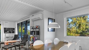 Een moderne kantoorruimte met een houten tafel, witte stoelen, een bureau met een computer, een boekenkast en een groot raam met uitzicht op bomen.