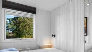 Een slaapkamer met twee bedden, een raam met uitzicht op bomen en een wandlamp.