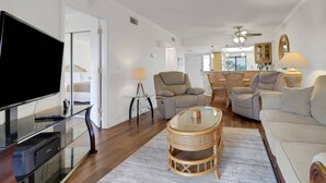 A modern living room with a flat-screen TV, comfortable seating, a dining area, and a kitchen in the background. - 21400 Bay Village Dr 204 (Fort Myers Beach)