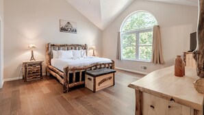 A bedroom with a wooden bed, a nightstand, a dresser, a large window, and a ceiling fan. - The Hangout Haven - theater, pickleball, ping pong, hot tub, karaoke, games (Long Pond)