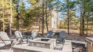 An outdoor seating area with Adirondack chairs and a stone fire pit. - The Hangout Haven - theater, pickleball, ping pong, hot tub, karaoke, games (Long Pond)