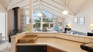 Un intérieur chaleureux avec une cheminée, un coin repas et de grandes fenêtres donnant sur le paysage extérieur.