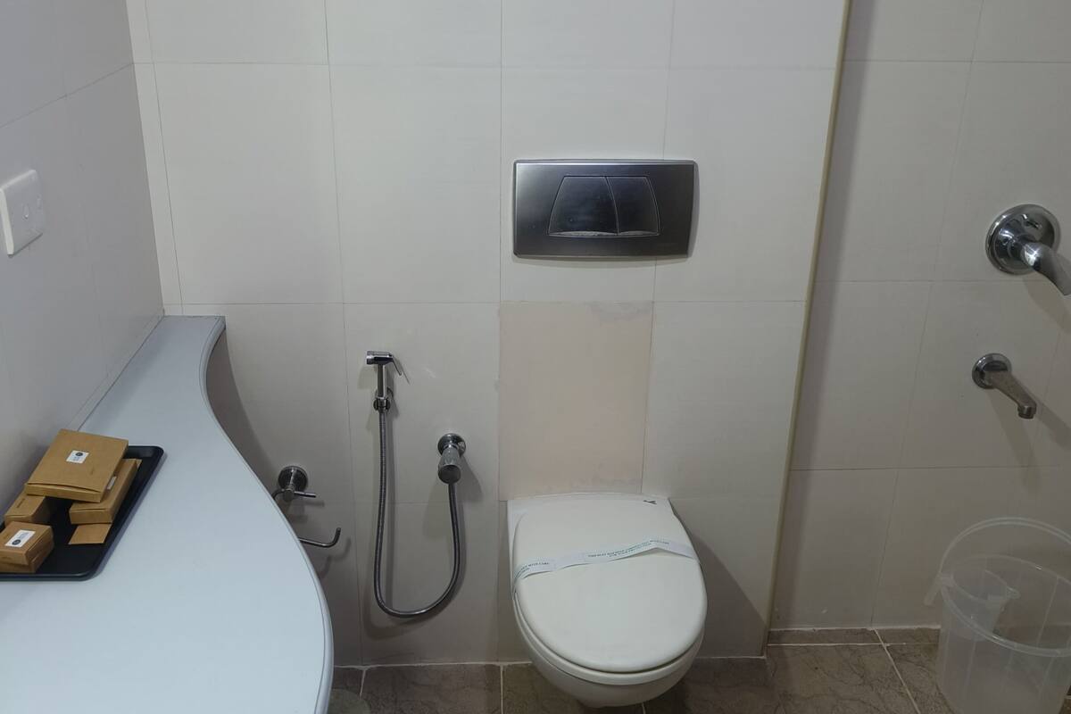A bathroom with a toilet, a shower, a sink with a tray of boxes, and a trash bin.