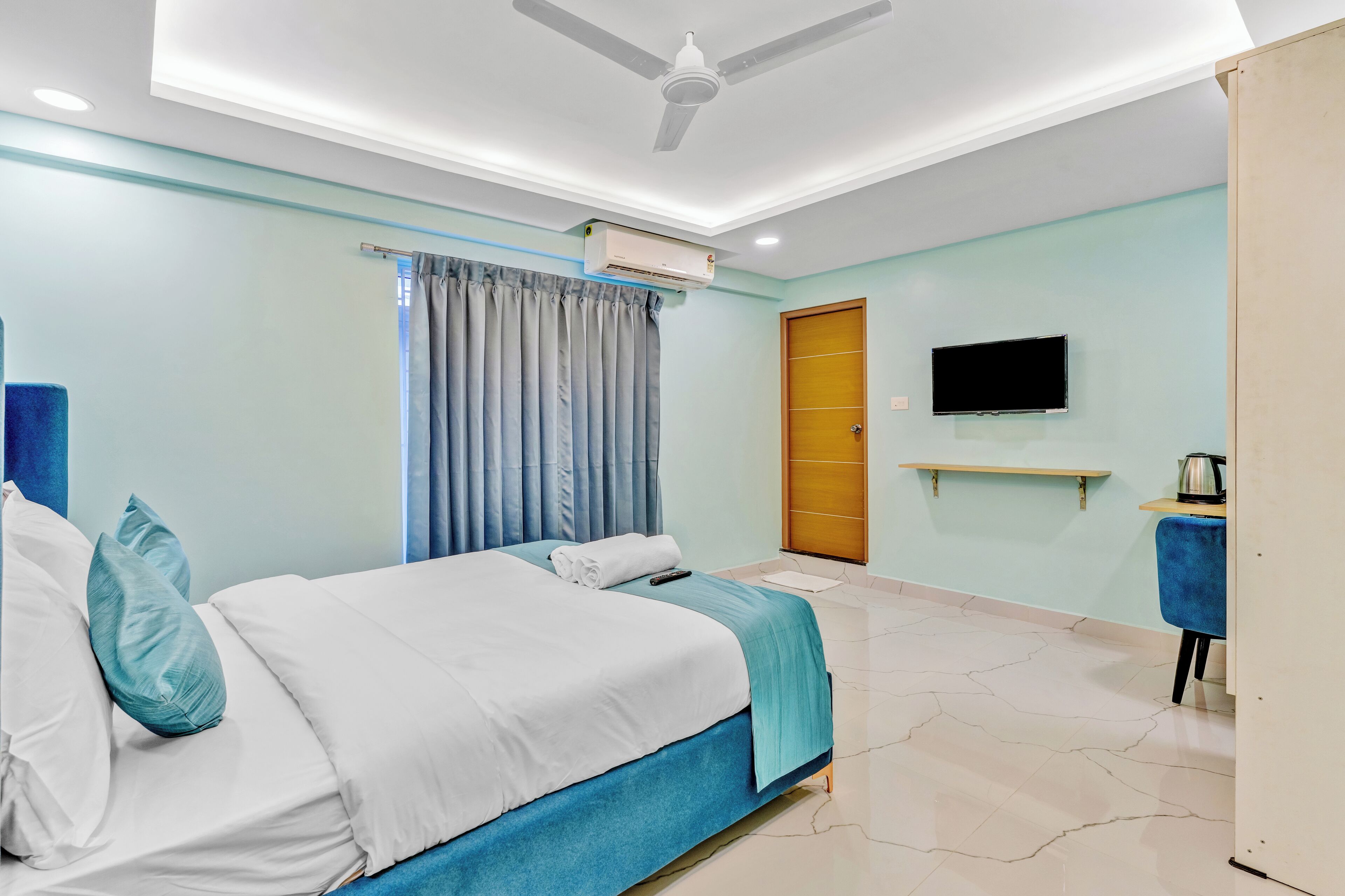 A hotel room with a bed, a TV, a ceiling fan, and a window with curtains.