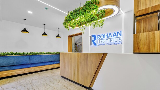 A hotel reception area with a wooden reception desk, a blue sofa, and a green plant hanging above the desk.