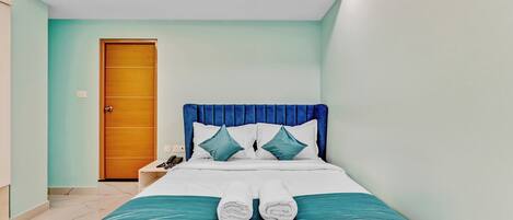 A neatly made bed with white linens and teal accents, a wooden door, and a nightstand with a phone.