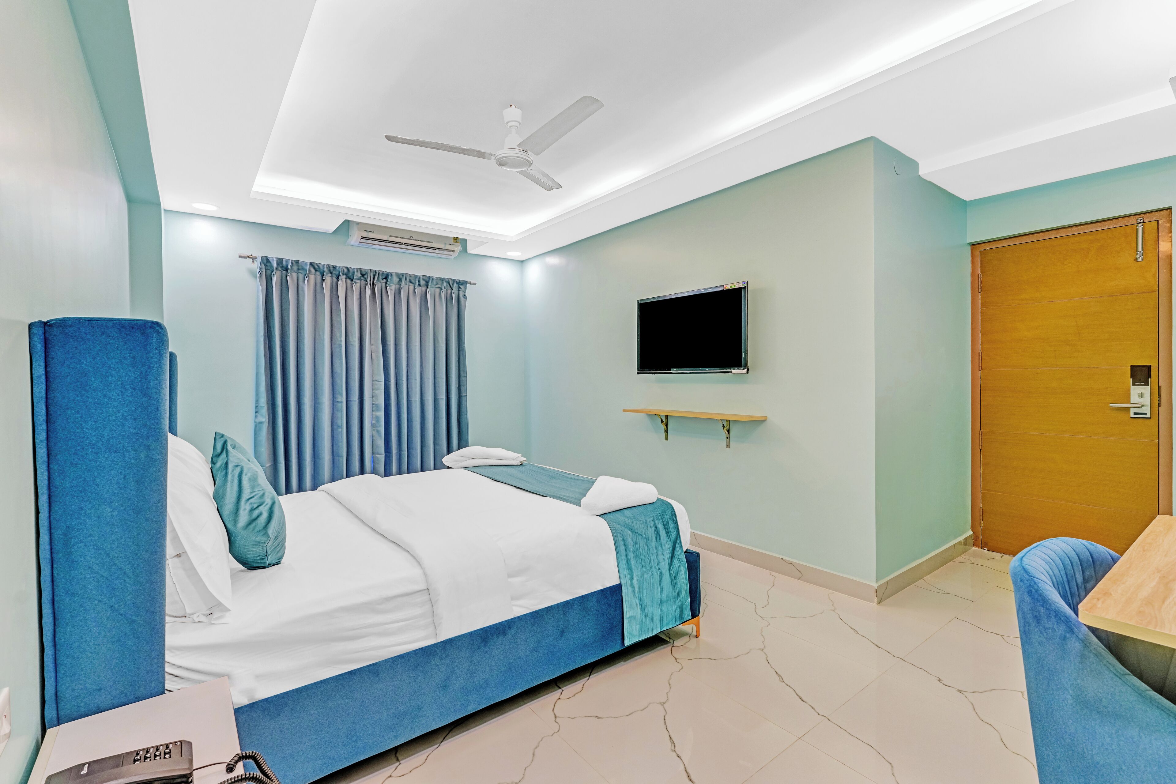 Una habitación de hotel con cama, escritorio, silla, televisor y puerta.