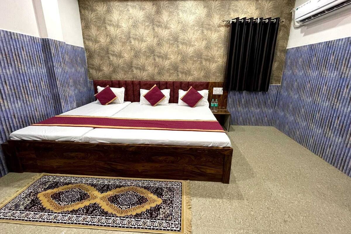 A hotel room with a bed, a nightstand, an air conditioning unit, and a patterned rug.