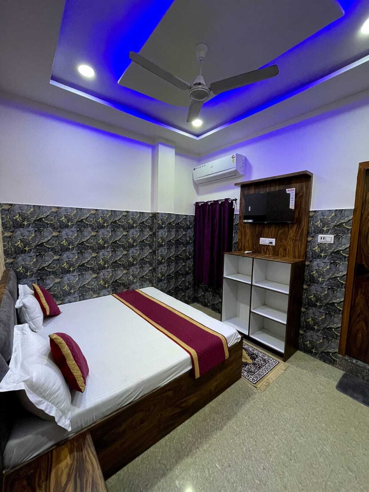 Habitación de hotel con cama, ventilador de techo, televisor montado y estante empotrado.