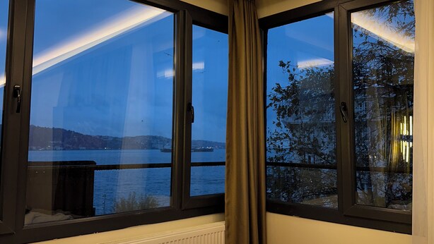 A hotel room with a large bed, two windows with curtains, a view of a body of water, and a radiator under the windows. - Lokka Hotel (Istanbul)