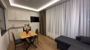 A modern living room with a sofa, a dining table with chairs, a TV mounted on the wall, and a kitchen area with cabinets and a sink. - Lokka Hotel (Istanbul)