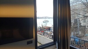 A room with a large window overlooking a body of water, a dock, and a cityscape. - Lokka Hotel (Istanbul)