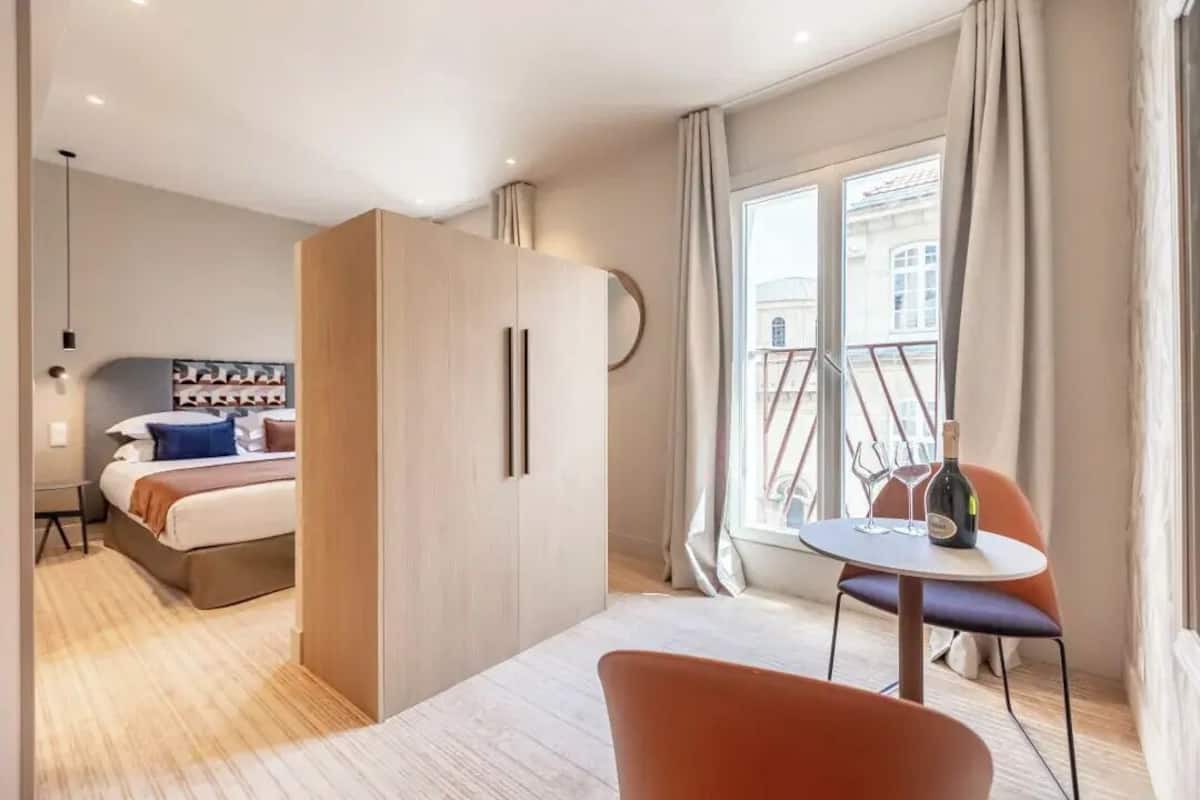 A modern hotel room with a bed, wardrobe, and a balcony with a table and chair.