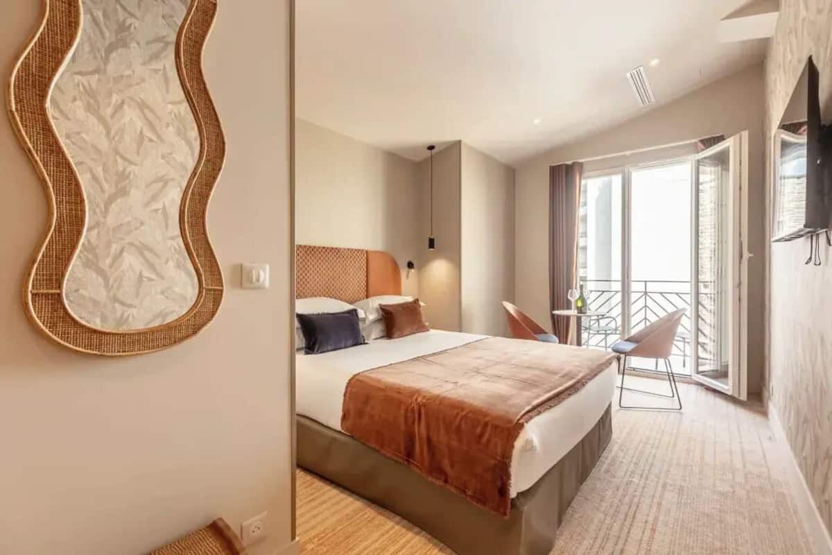 A modern hotel room with a large bed, a balcony with a chair, and a wall-mounted TV.