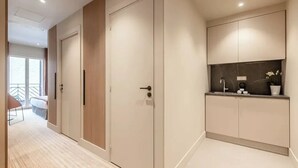 A modern hotel room with a large wardrobe, a built-in vanity with a mirror, and a small seating area with a chair and table. - Suites FL by Sweett (Paris)