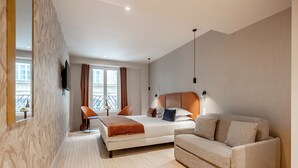 A modern hotel room with a bed, a sofa, a TV mounted on the wall, and a window with curtains. - Suites FL by Sweett (Paris)