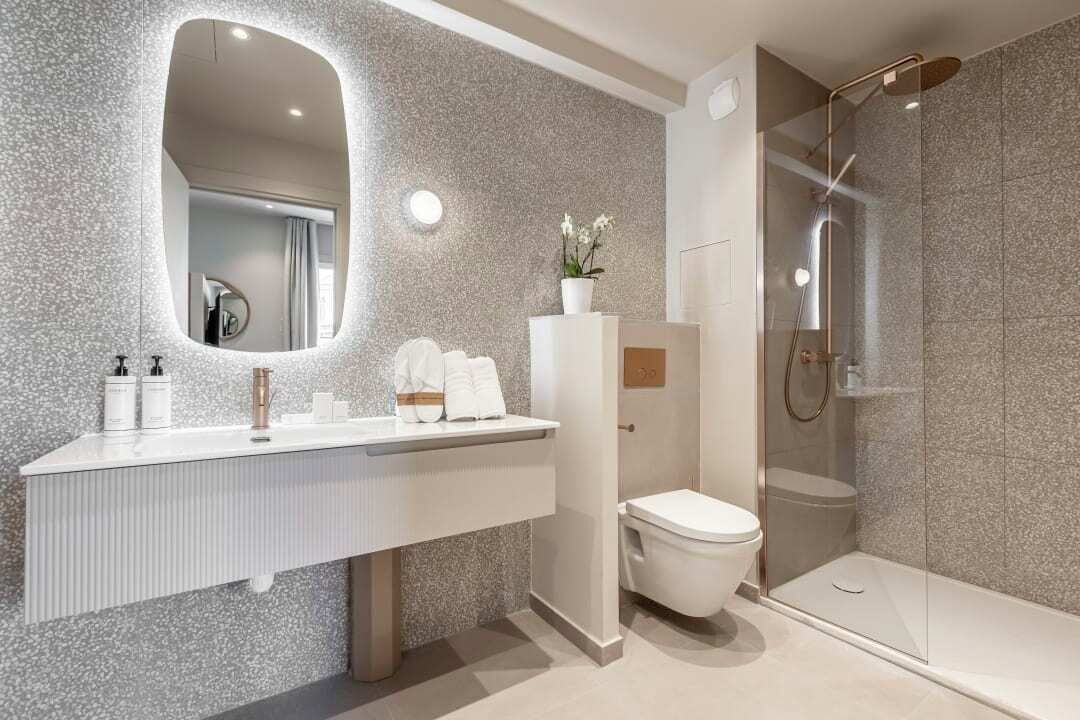 A modern bathroom with a granite countertop, a large mirror, a toilet, and a glass-enclosed shower area.