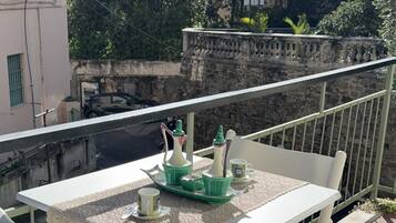 Un balcone con tavolo e sedie, vista su una strada e un edificio sullo sfondo.