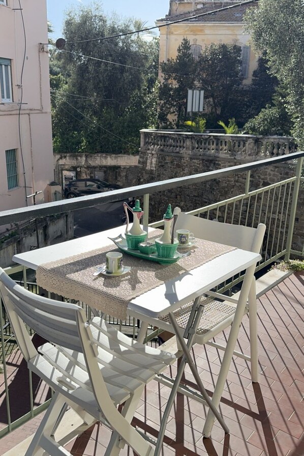 Un balcone con tavolo e sedie, vista su una strada e un edificio sullo sfondo.