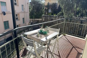 Un balcon avec une table et des chaises, une balustrade et une vue sur des immeubles et des arbres.