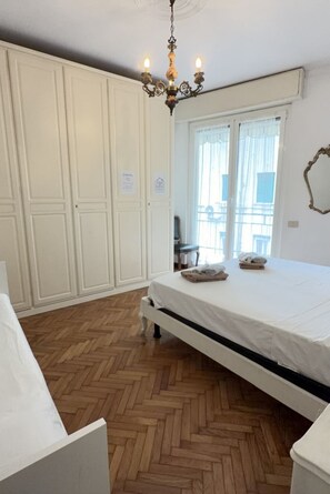 Una camera da letto con un letto, un comò, una lampada a sospensione e una finestra con tende.