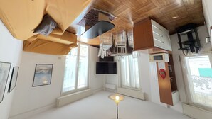 A room with a wooden ceiling, a flat-screen TV, a standing lamp, and a window with a view. - [200m from the Sea] 3 min from Porto Sole (Sanremo)