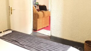 Una habitación de hotel con una cama, una puerta que da a una sala de estar con una computadora portátil, y un plato decorativo en la pared.