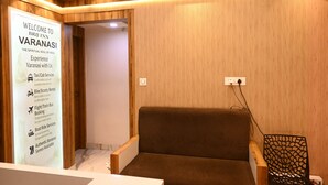 A reception area with a wooden wall, a brown sofa, and a signboard detailing services like taxi, cab, bike rental, and booking assistance. - Brij Inn (Varanasi)