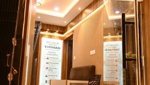 A reception area with a glass door, a reception desk, a sofa, and a chair. There are signs with information about the hotel's services. - Brij Inn (Varanasi)